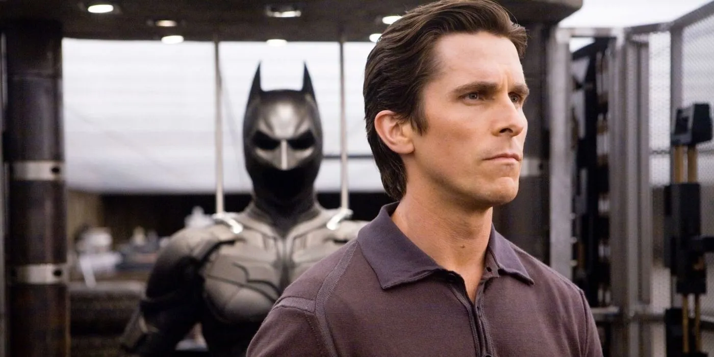 Bruce Wayne looking serious while standing in front of his Batman suit in The Dark Knight