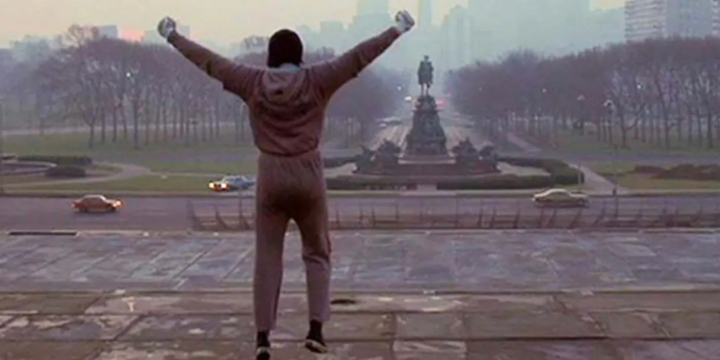Rocky at the top of the stairs from Rocky III, jumping up hands in the air.